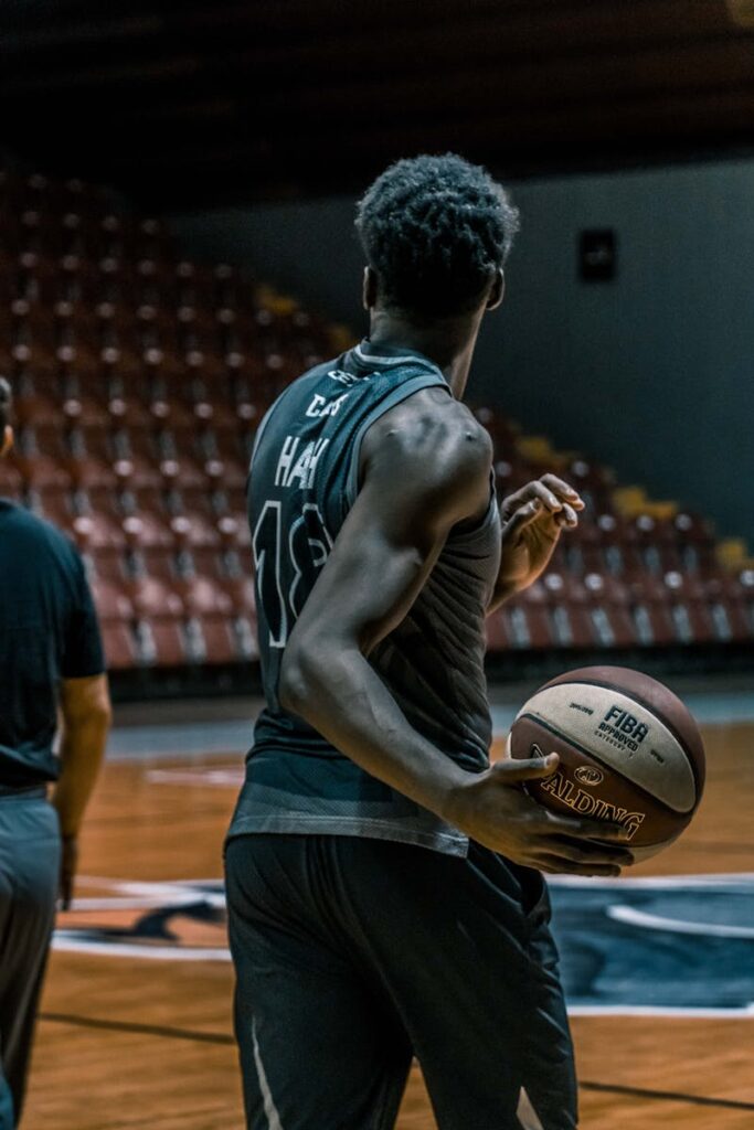 Athlete in jersey practicing basketball in indoor stadium holding a ball.