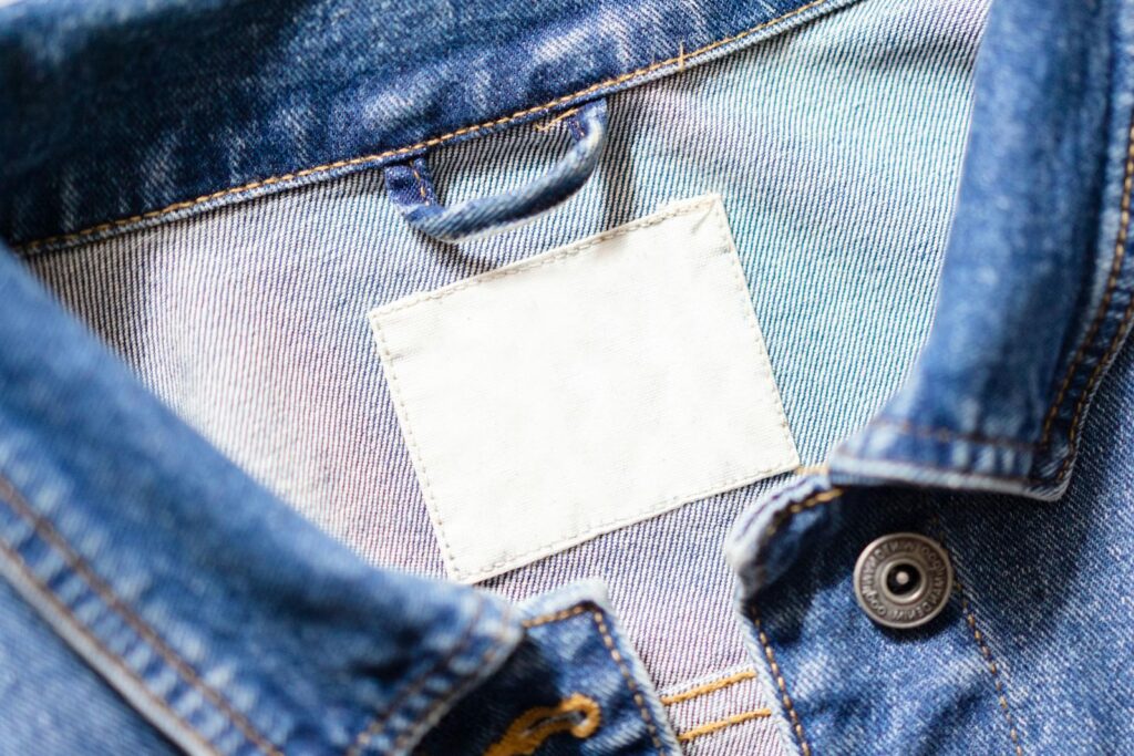 Close-up shot of a denim jacket's collar featuring a blank white tag and detailed stitching.