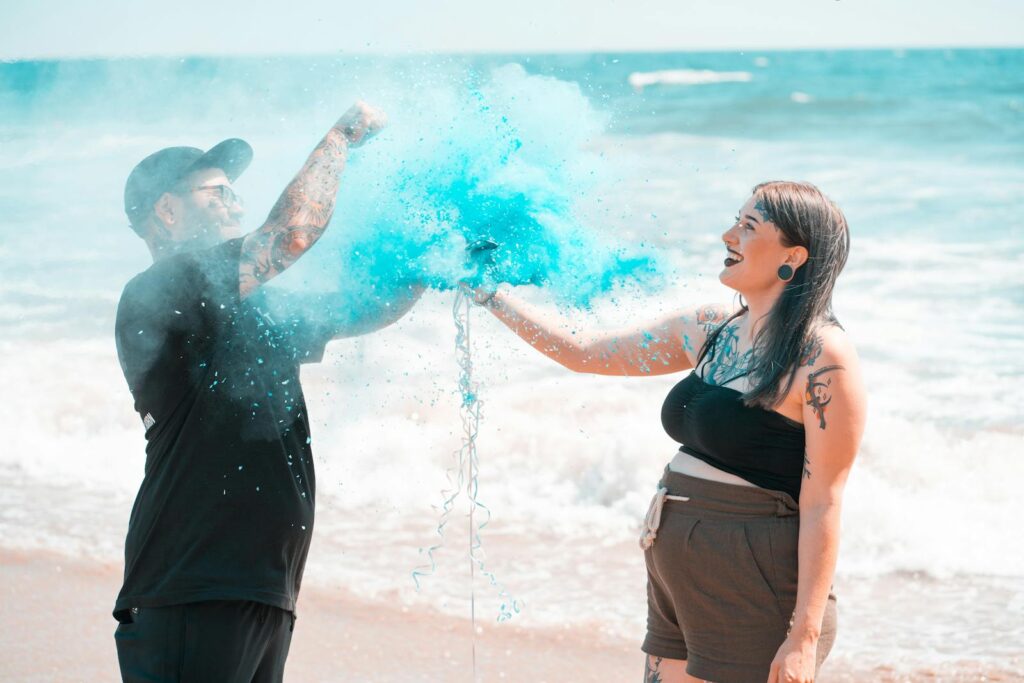 Happy couple celebrates gender reveal with blue powder on Santa Monica beach.