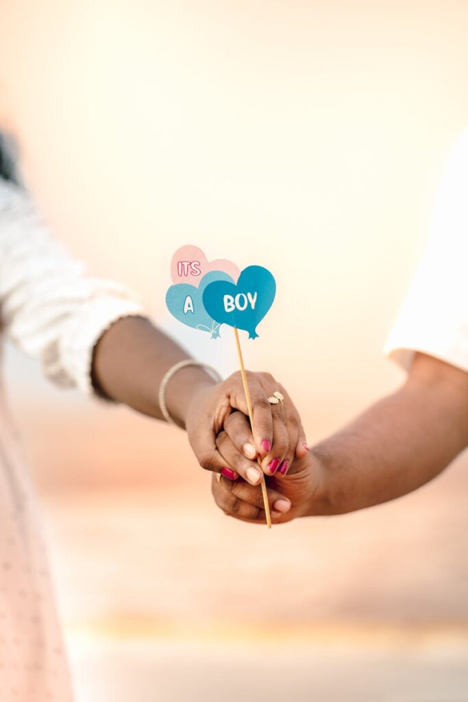 Joyful couple's hands holding 'It's a Boy' sign, announcing pregnancy on a sunny beach.