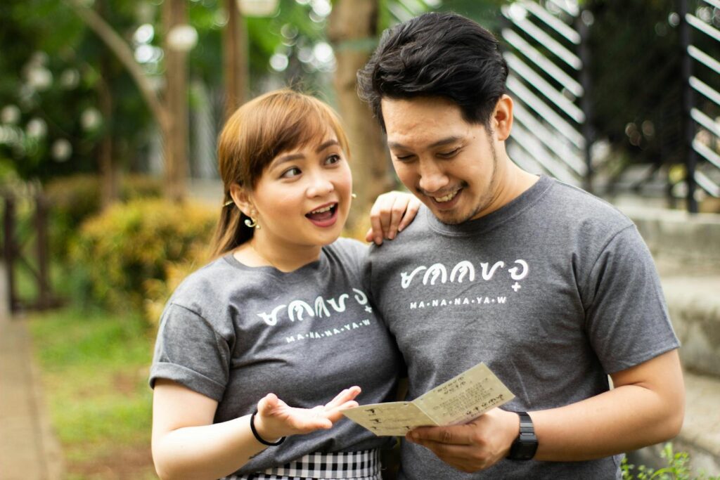 A happy couple in matching shirts smiles while reading a card outdoors.