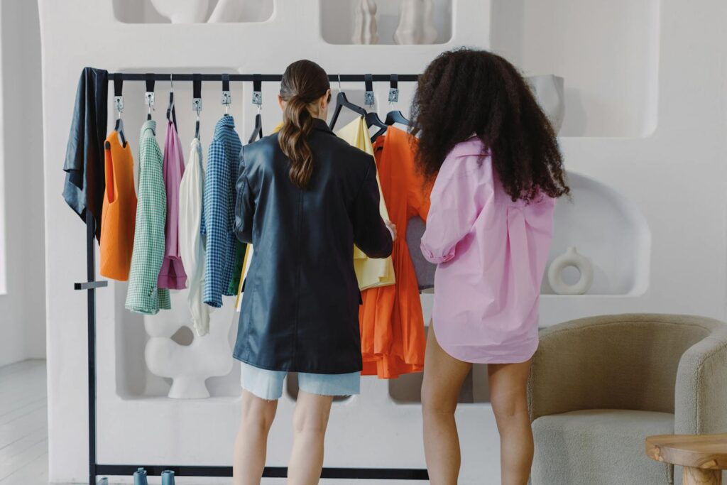 Two women selecting vibrant clothes on a rack indoors, showcasing fashion choices.