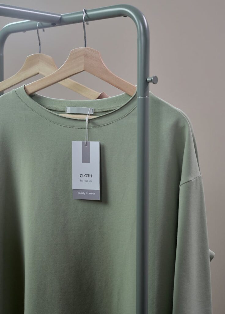 Close-up of a green shirt on a hanger with label tag on a minimalist clothing rack.