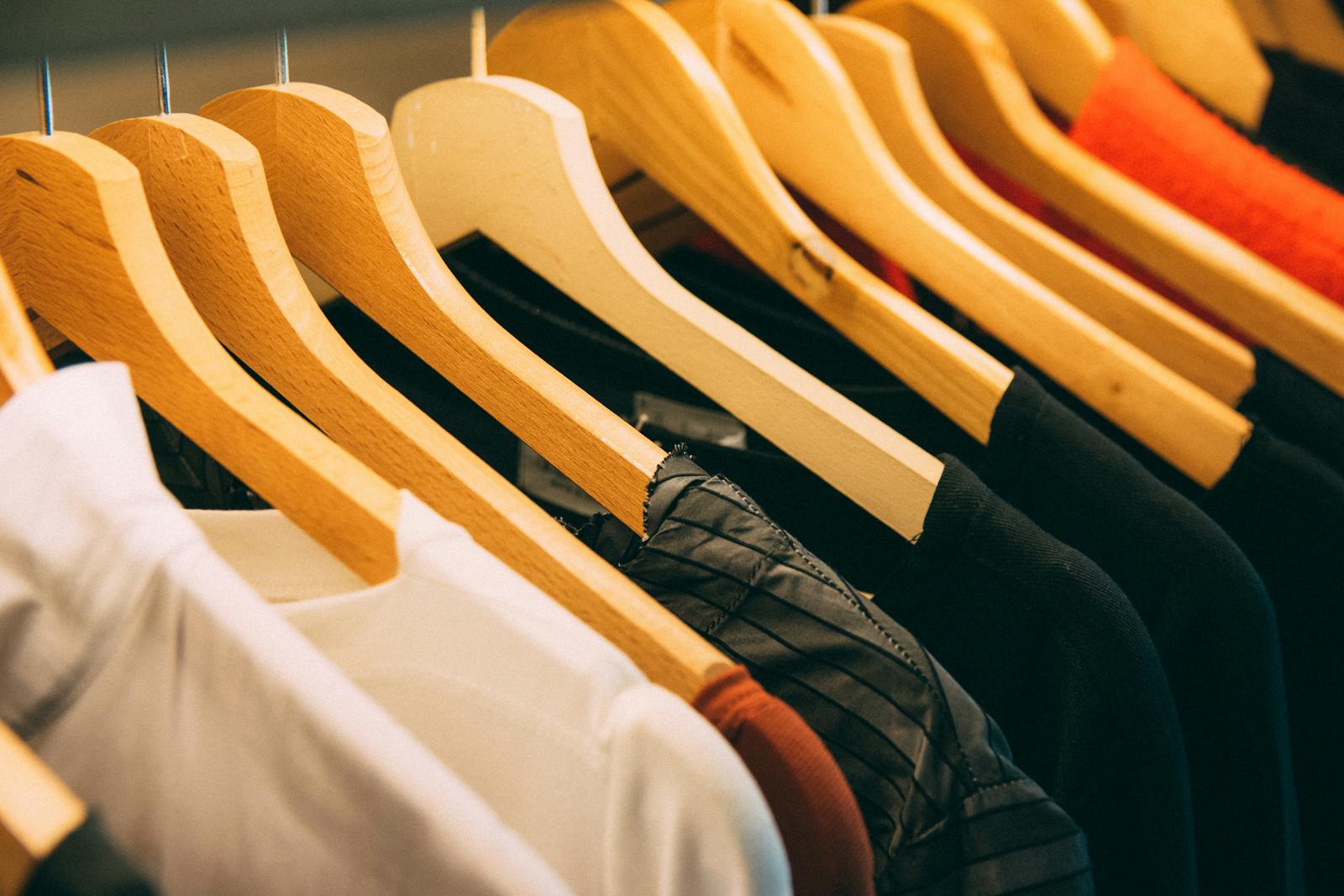 A close-up view of a row of clothes on wooden hangers, showcasing various fabrics and colors in a wardrobe setting. types of necklines on shirts
