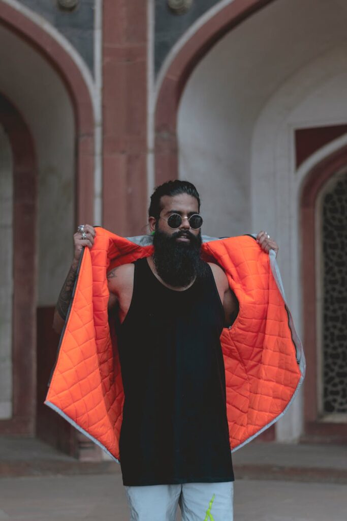 Stylish adult male posing with a striking orange vest in an elegant archway.