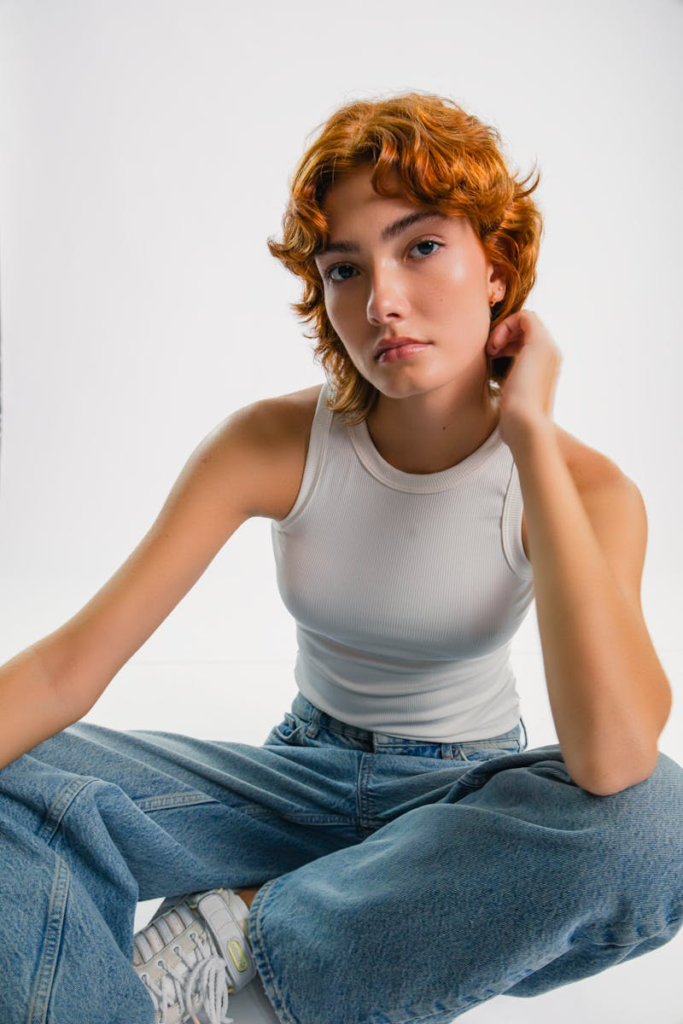 Portrait of a young adult seated casually wearing denim jeans and a white tank top.
