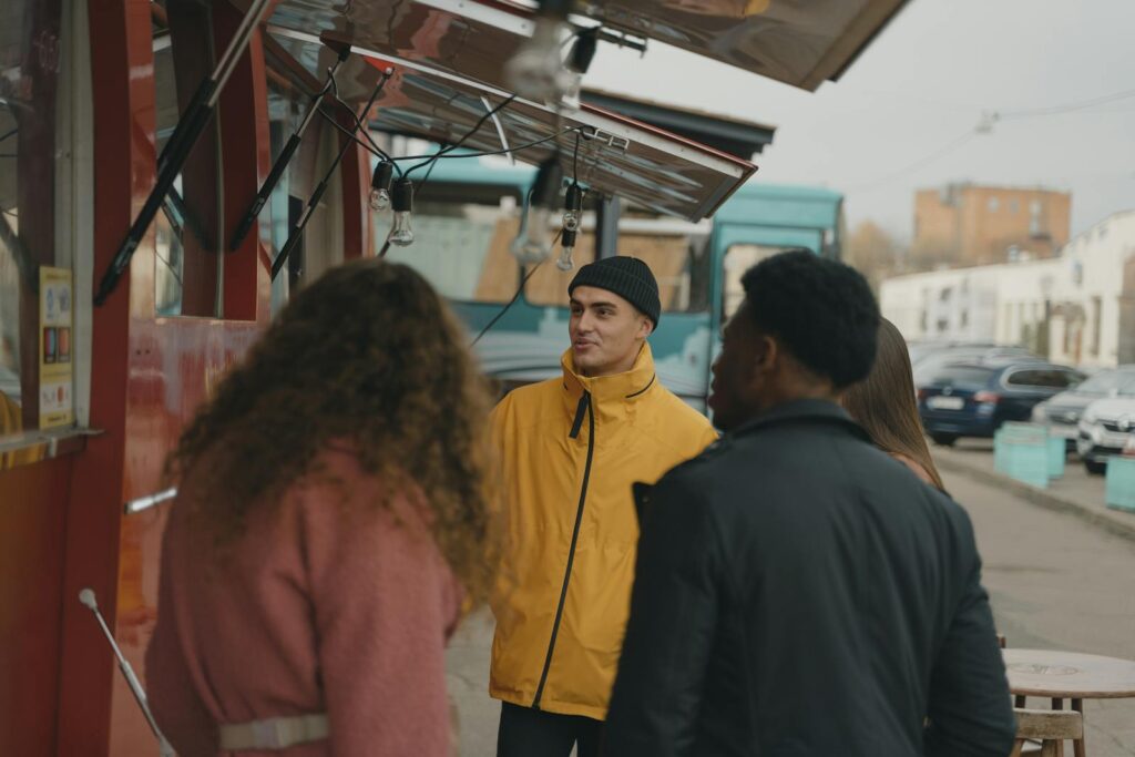 A group of friends enjoying a casual day at an outdoor food truck with hanging string lights.