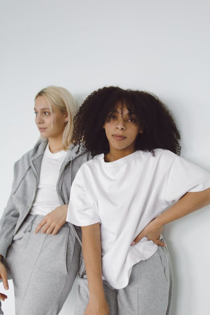 Two women in casual loungewear posing against a white wall, showcasing relaxed fashion indoors.