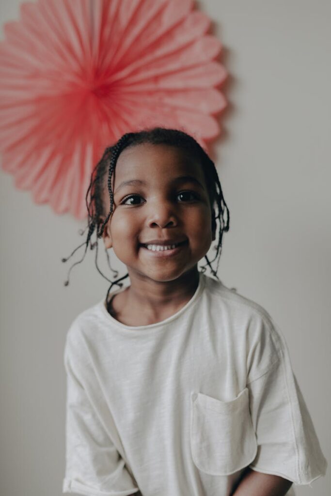 Adorable smiling child with braids wearing a white t-shirt indoors.
