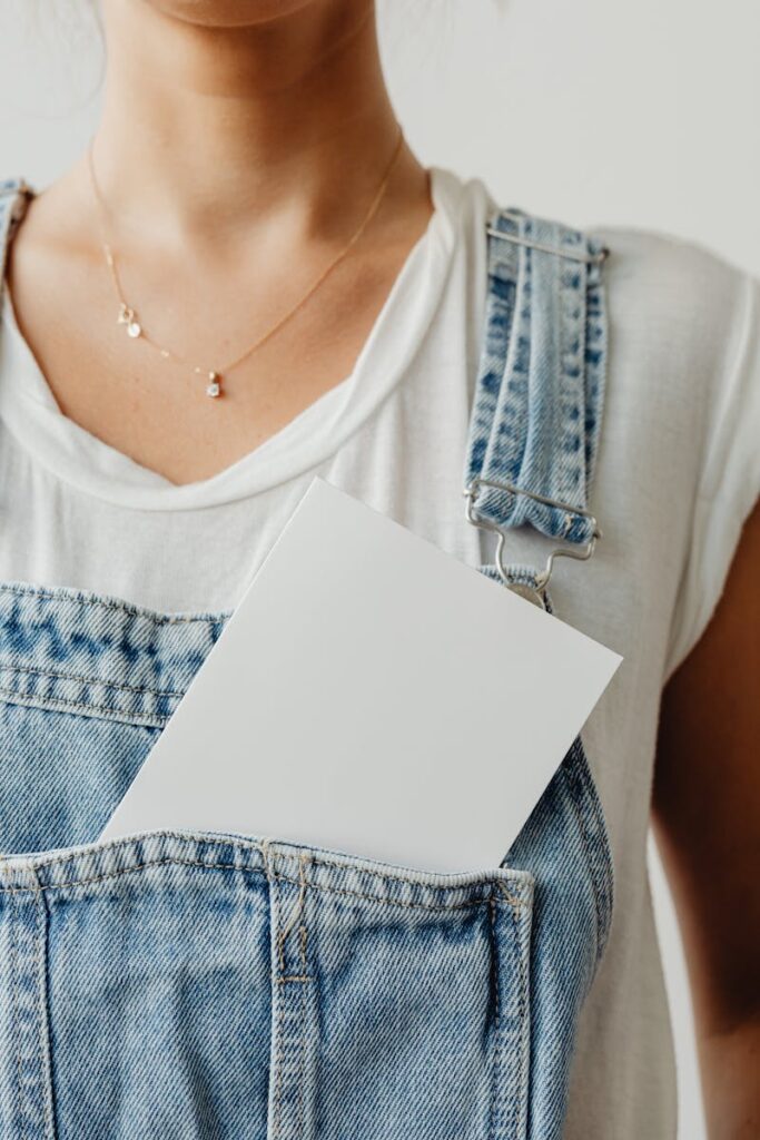 Close-up of a person wearing denim overalls with a blank card in the pocket, showcasing a casual style.