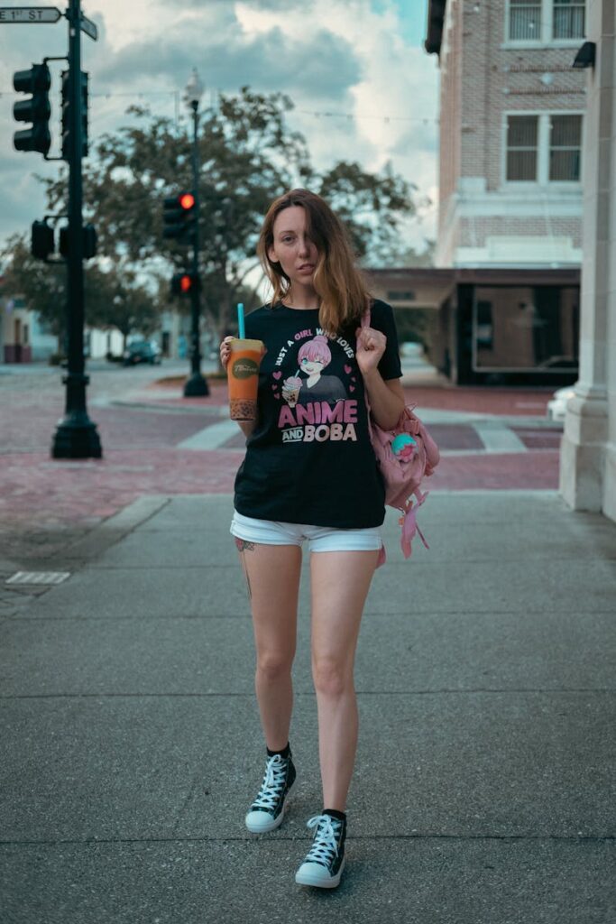 Stylish woman in casual attire drinks boba tea while walking on an urban street during summer.
