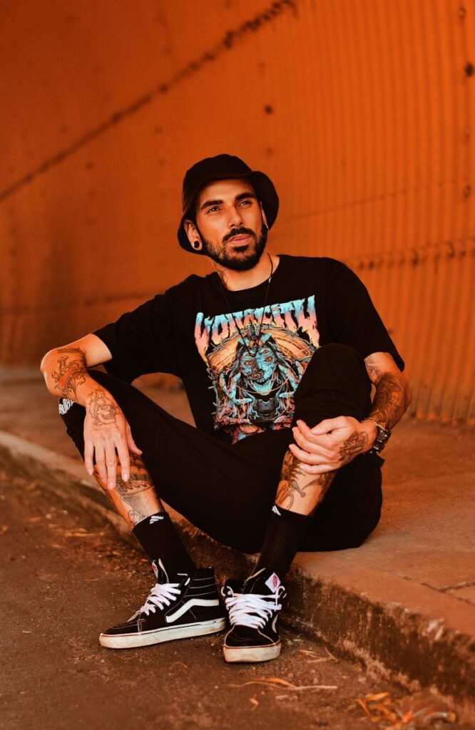 Portrait of a tattooed man sitting in a vibrant orange urban setting, showcasing youth culture.