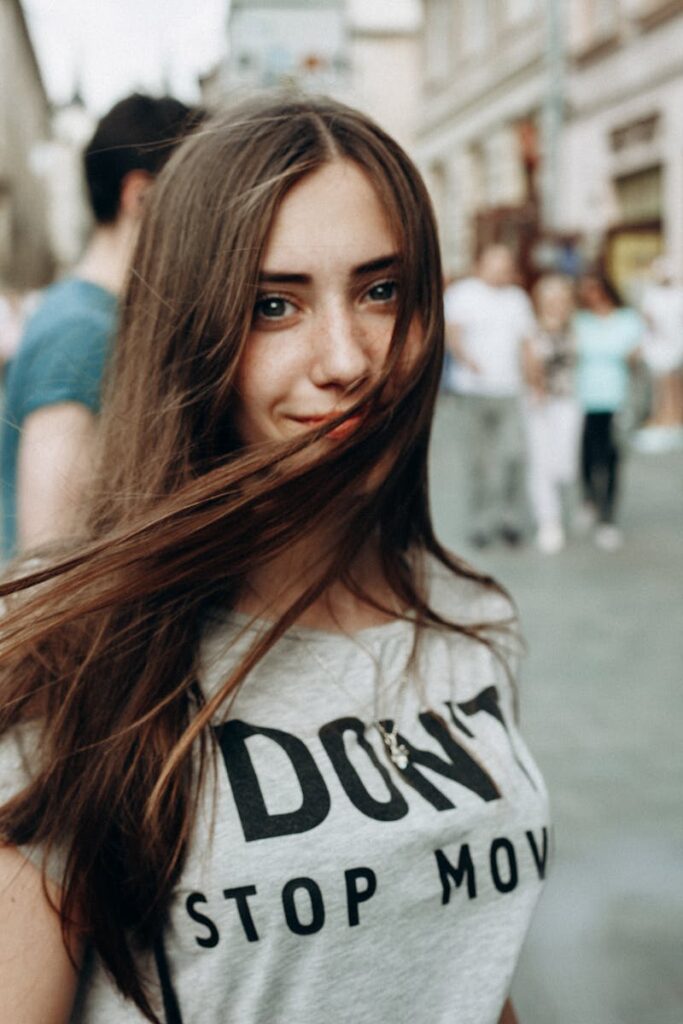 Young woman with flowing hair smiles in an urban street setting, creating a dynamic and lively portrait.