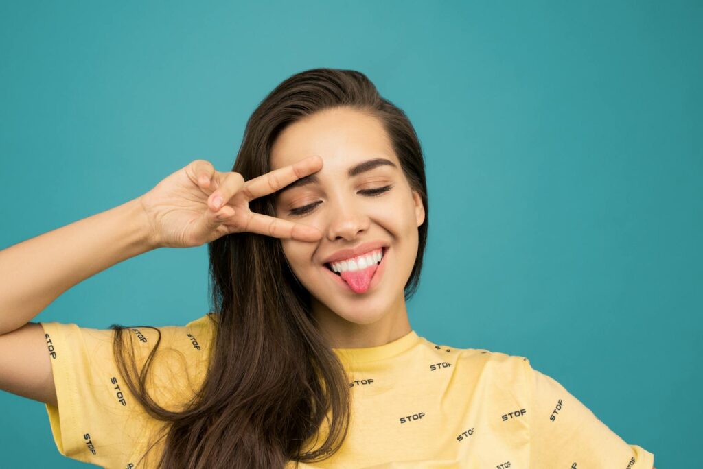 Cheerful young woman posing with a playful hand gesture and sticking her tongue out.