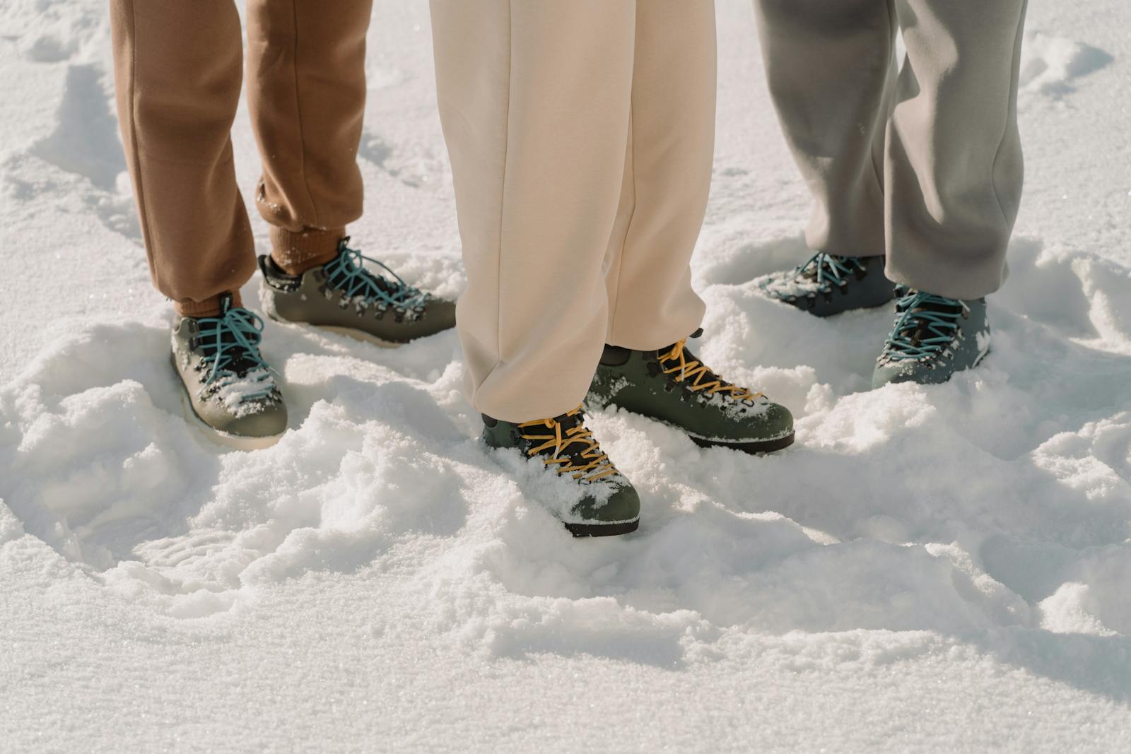 Close-up of three people wearing boots in snow, showcasing winter fashion footwear. Champion Sweatpants