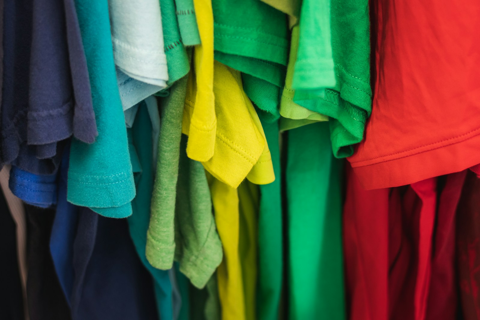 a bunch of colorful shirts hanging on a rack (DTF Transfers) vs. Screen Printing vs. DTG: Which Is Best for Your Brand?