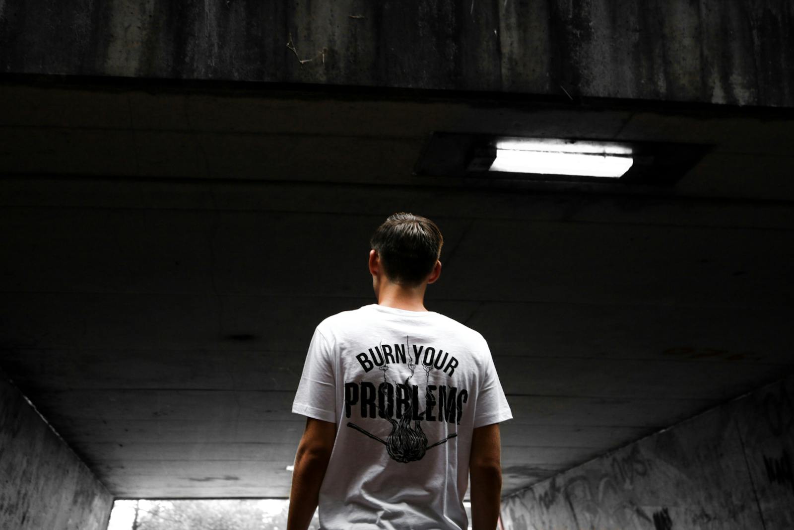 Photo by Sebastiaan Stam A man stands in an urban tunnel wearing a t-shirt with a bold statement.
