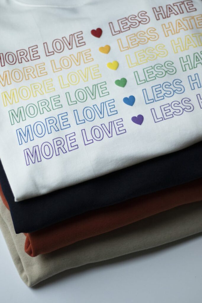 Stack of rainbow-themed shirts with 'More Love, Less Hate' message.