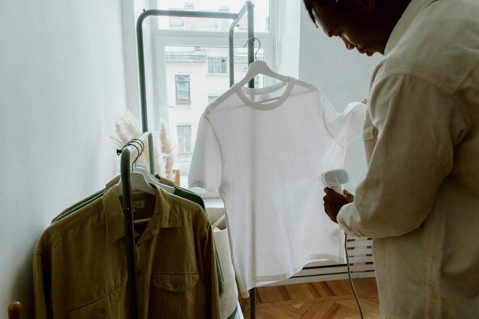 Photo by Ron Lach A man uses a steam iron on a white shirt hanging from a clothing rack indoors.