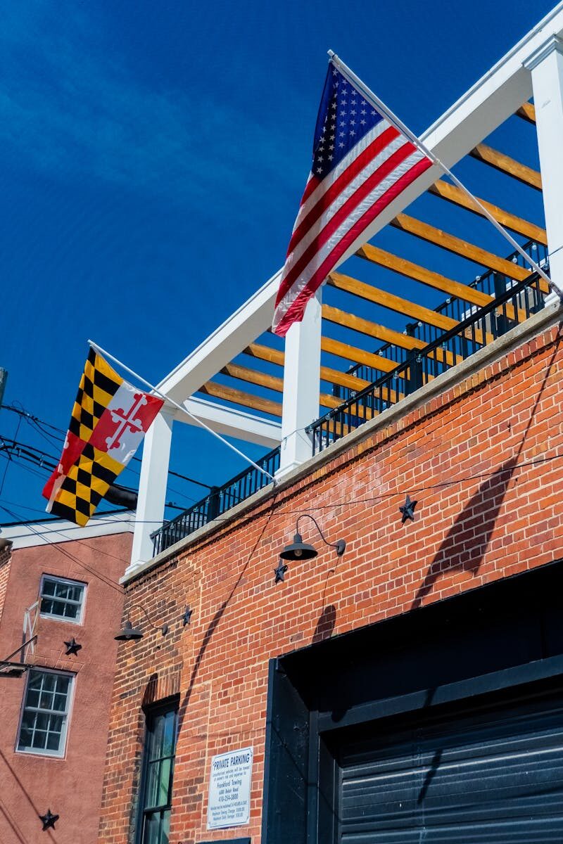 Photo by Tranise Foster American and Maryland flags on brick building under a clear blue sky.