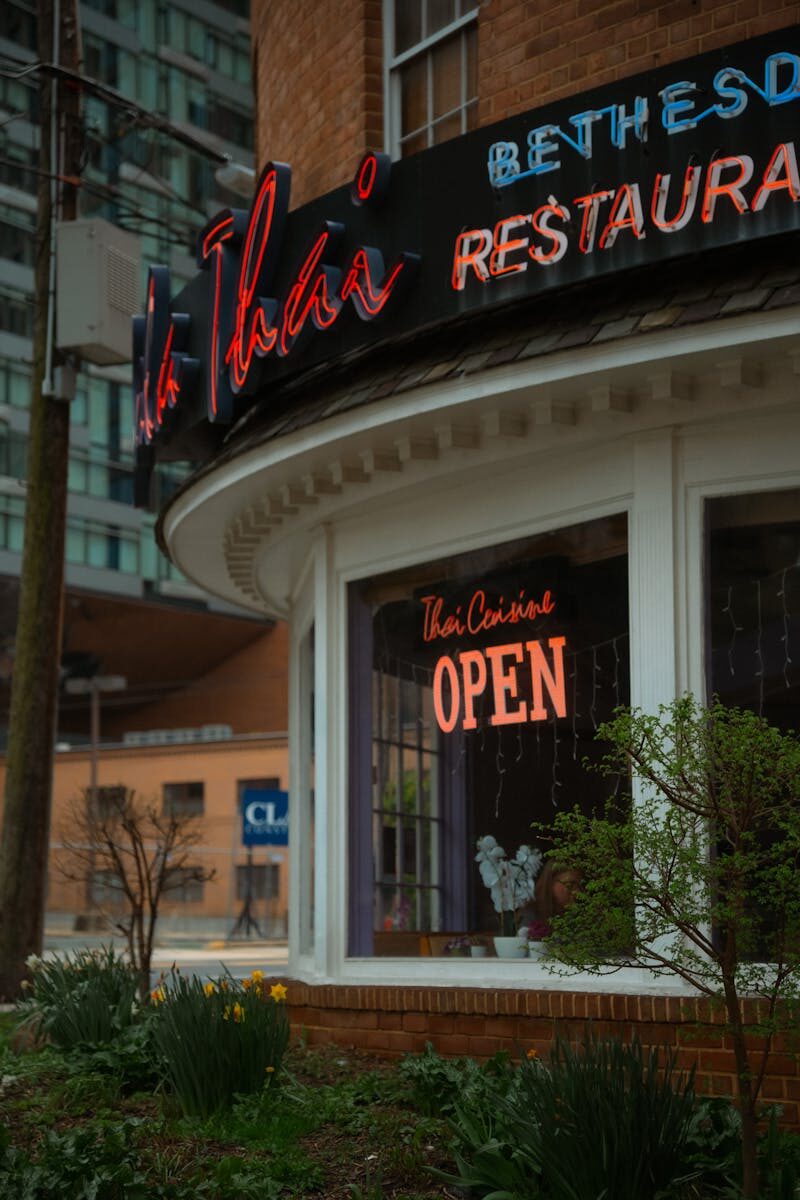 Photo by Daniela Sánchez Street view of a Thai restaurant in Bethesda, Maryland with neon 'Open' sign.