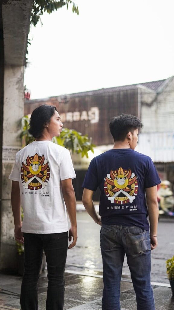 Two men stand outdoors showcasing graphic t-shirts with unique sun design in an urban setting.
