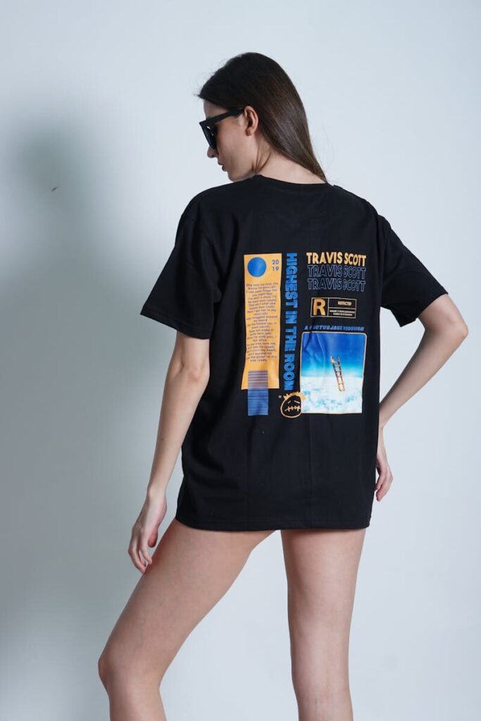 Fashionable young woman posing in graphic t-shirt and sunglasses in studio setting.