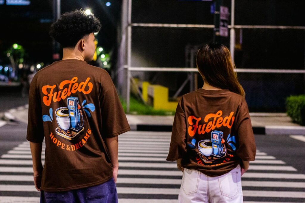 Couple wearing graphic T-shirts crossing a city street at night, showcasing urban fashion.