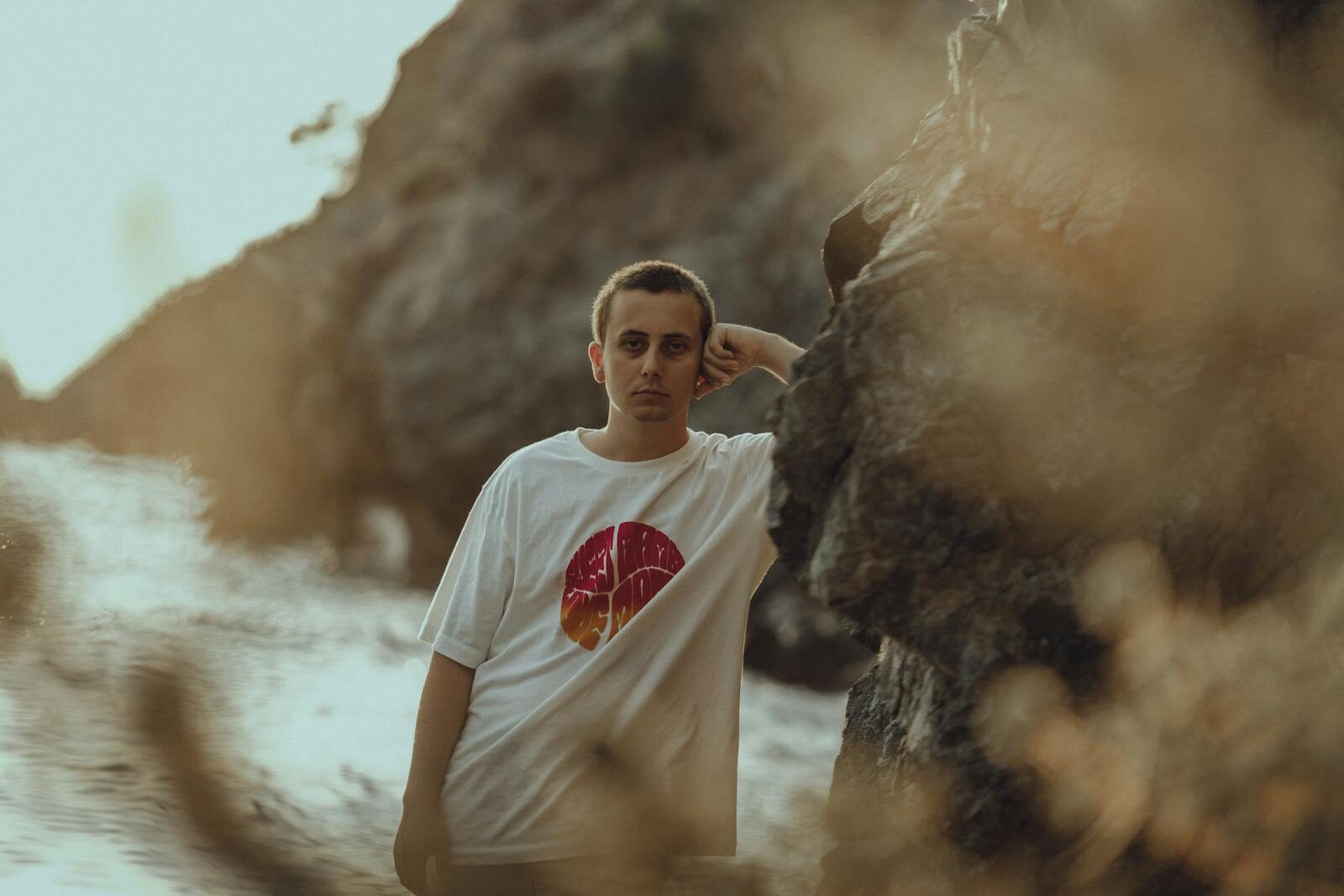 A young man in a t-shirt leans against a rocky cliff by the seaside, with a blurred background of waves. DTF Transfers Mistakes: 10 Errors That Ruin Your Prints