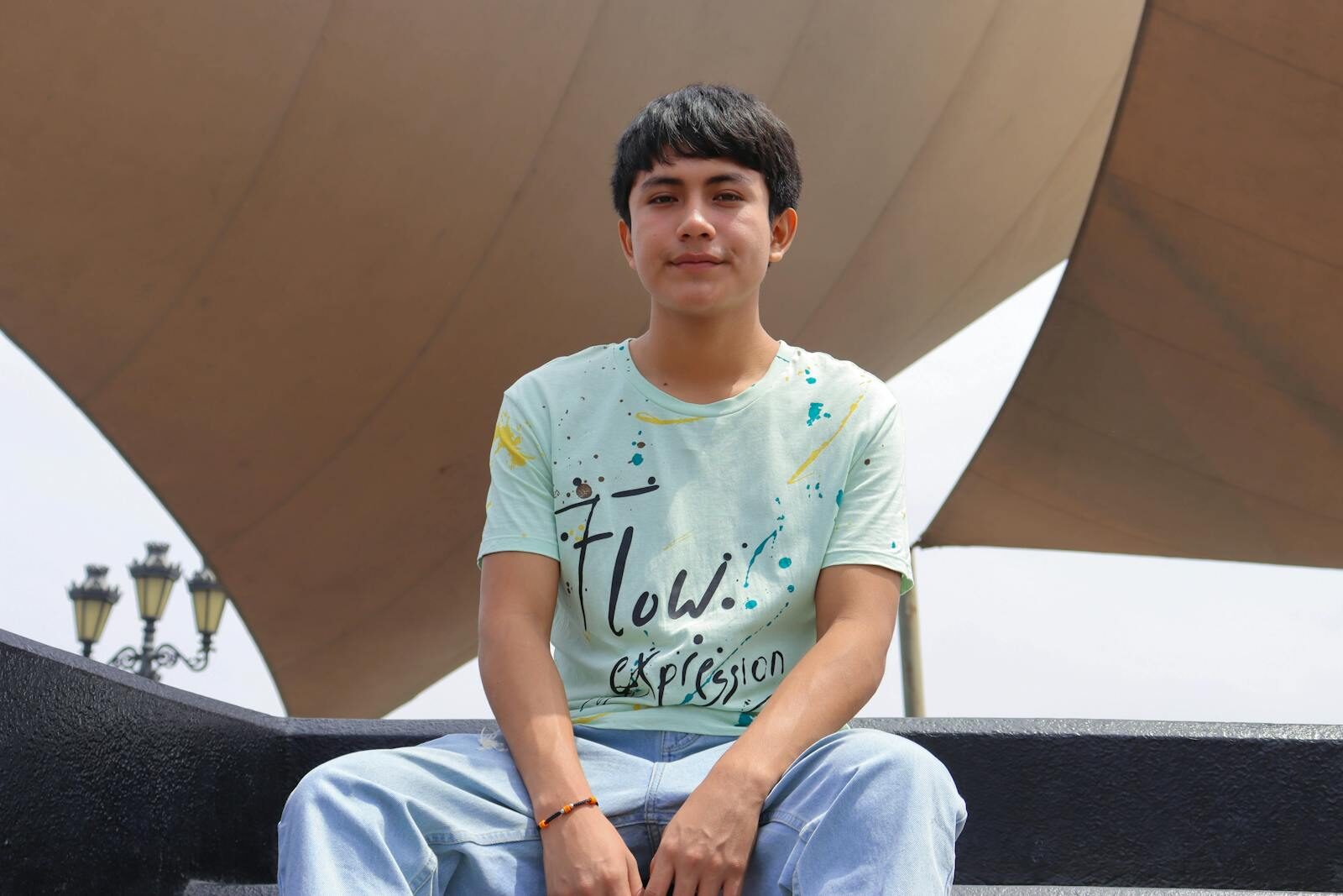 A young man posing outdoors in a casual tee and jeans with urban architecture background. DTF Transfers vs Sublimation: Key Differences Explained
