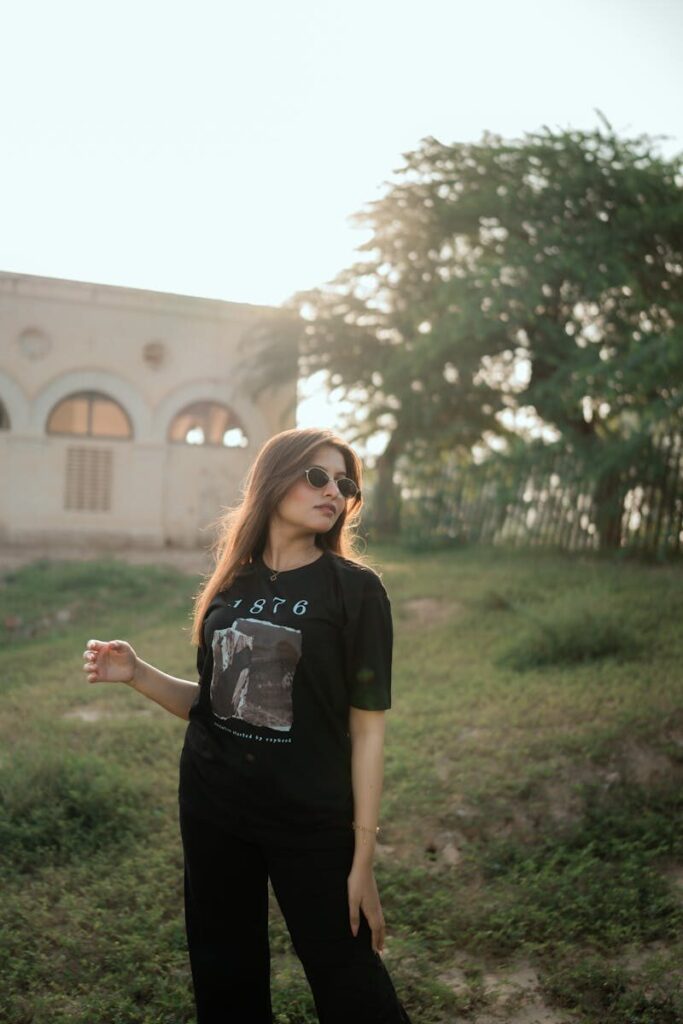 Stylish young woman wearing sunglasses standing outdoors in natural sunlight, exuding a casual and confident vibe.