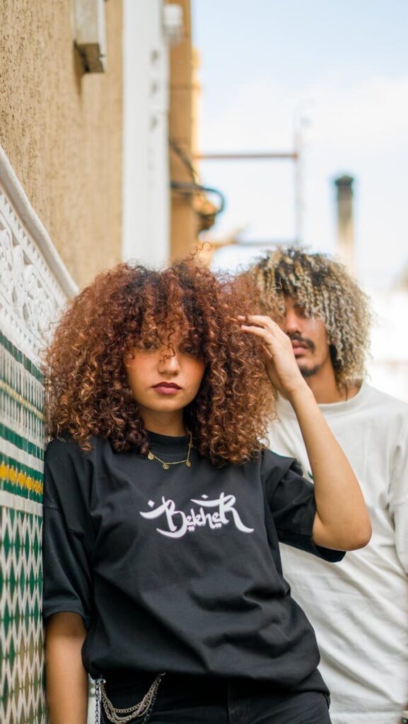 Portrait of two stylish young adults with curly hair in urban setting, showcasing modern fashion.