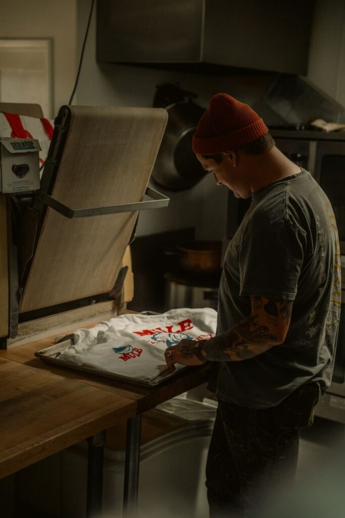 Adult man printing a custom t-shirt using a heat press in a dimly lit workshop.