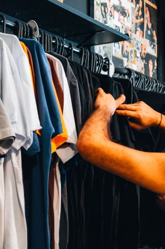 A person browsing a colorful selection of t-shirts in a clothing store, showcasing diverse fashion choices.